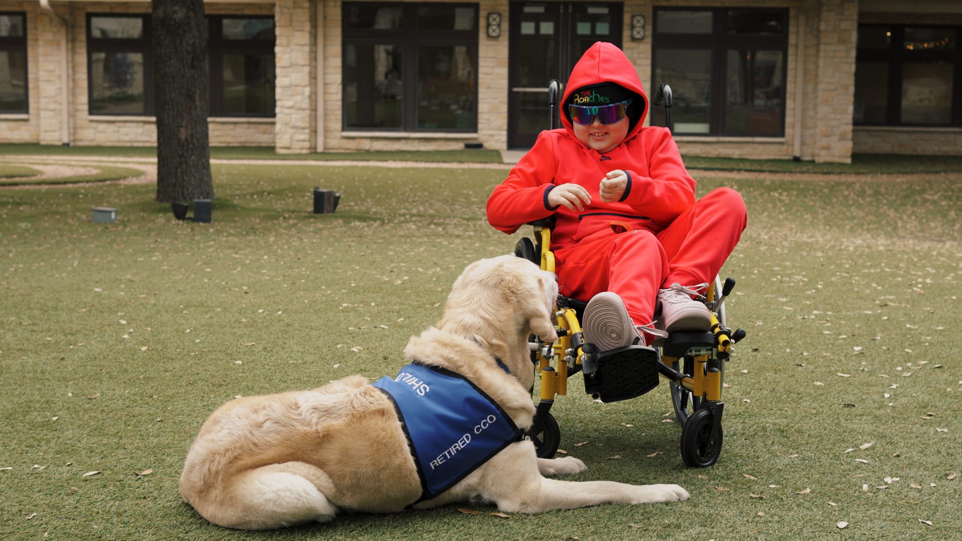 Child in a red jacket with a service dog in the courtyard