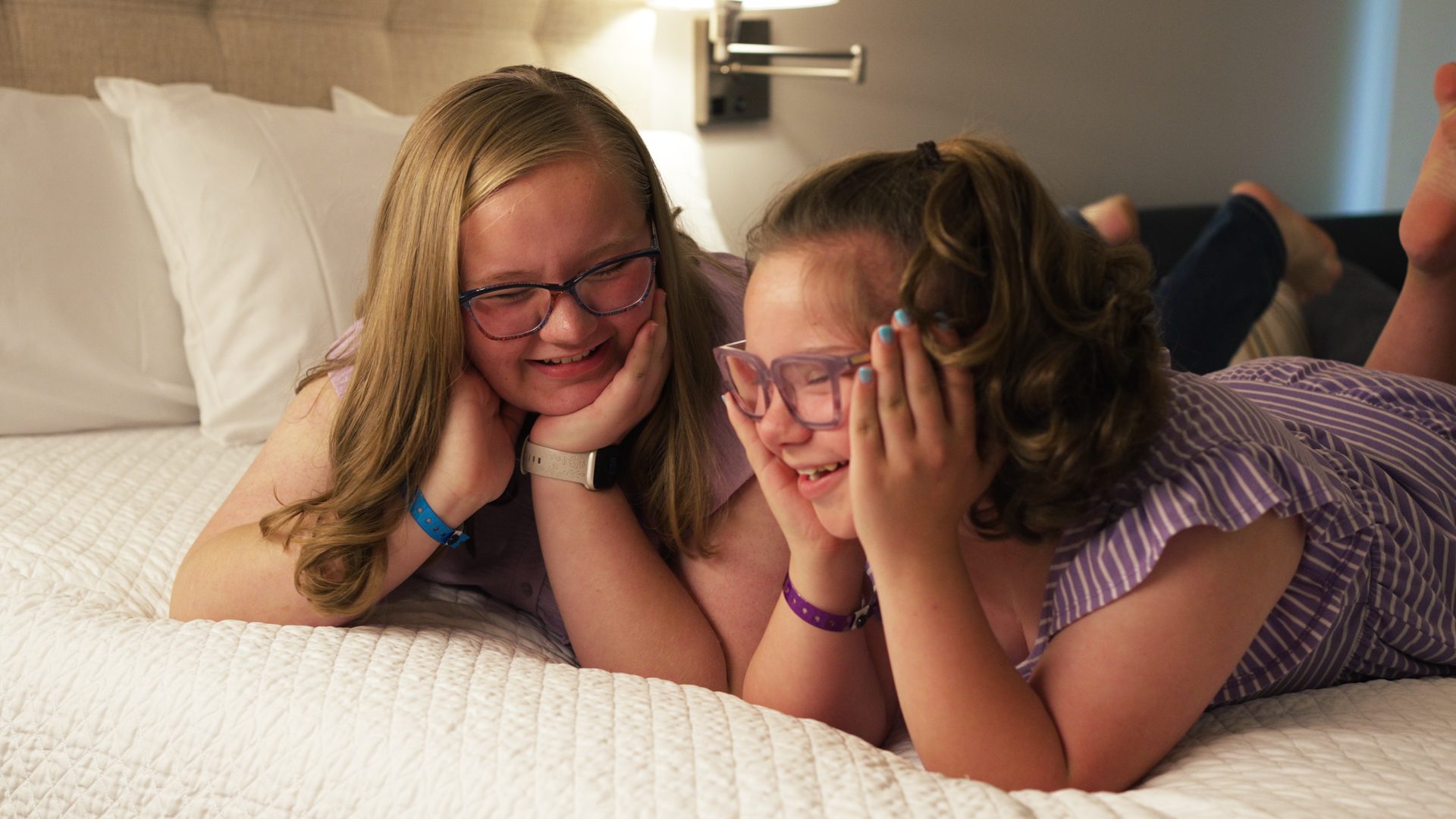Two sisters smiling on a bed at Ronald McDonald House Dallas